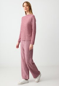 Top rosa lavorato a maglia con un motivo zigzag testurizzato, abbinato a pantaloni palazzo coordinati. Il modello indossa sneakers bianche. Design semplice e casual.