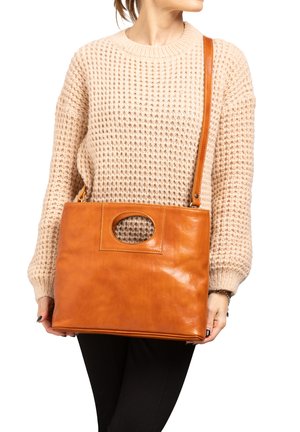 Femme portant un pull en maille beige tenant un grand sac à main rectangulaire en cuir marron clair avec une poignée ovale courte et une longue bandoulière.