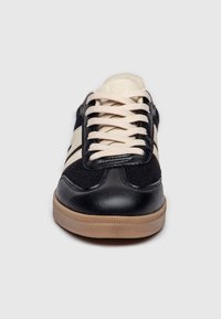 Sneaker nera in pelle e tessuto con lacci crema e due strisce crema sui lati. Suola in gomma con finitura testurizzata e punta arrotondata.