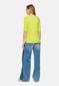 Limegrünes kurzärmliges Oberteil kombiniert mit hellblauen weit geschnittenen Jeans, die eine lockere Passform und klare Linien aufweisen.