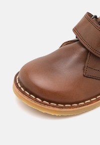 Brune lærersko med rund tå, med en syet såle og et borrelåsspenne på oversiden for enkel feste.