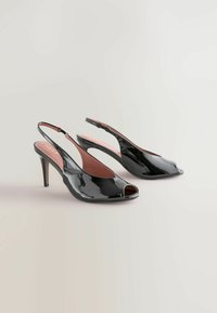 Czarne, lakierowane zamszowe sandały na obcasie z odkrytymi palcami i smukłym, średniej wysokości obcasem typu stiletto, prezentowane na jasnym tle.
