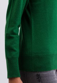 Grön stickad tröja med rund halsringning, ribbade ärmmuddar och nederkant. Tillverkad av ett mjukt, strukturerat material och har en rak skärning.