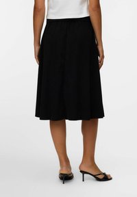 Jupe noire au genou en tissu doux avec une taille ajustée, dotée d'un design évasé et de lignes simples et épurées. Portée avec des talons noirs.