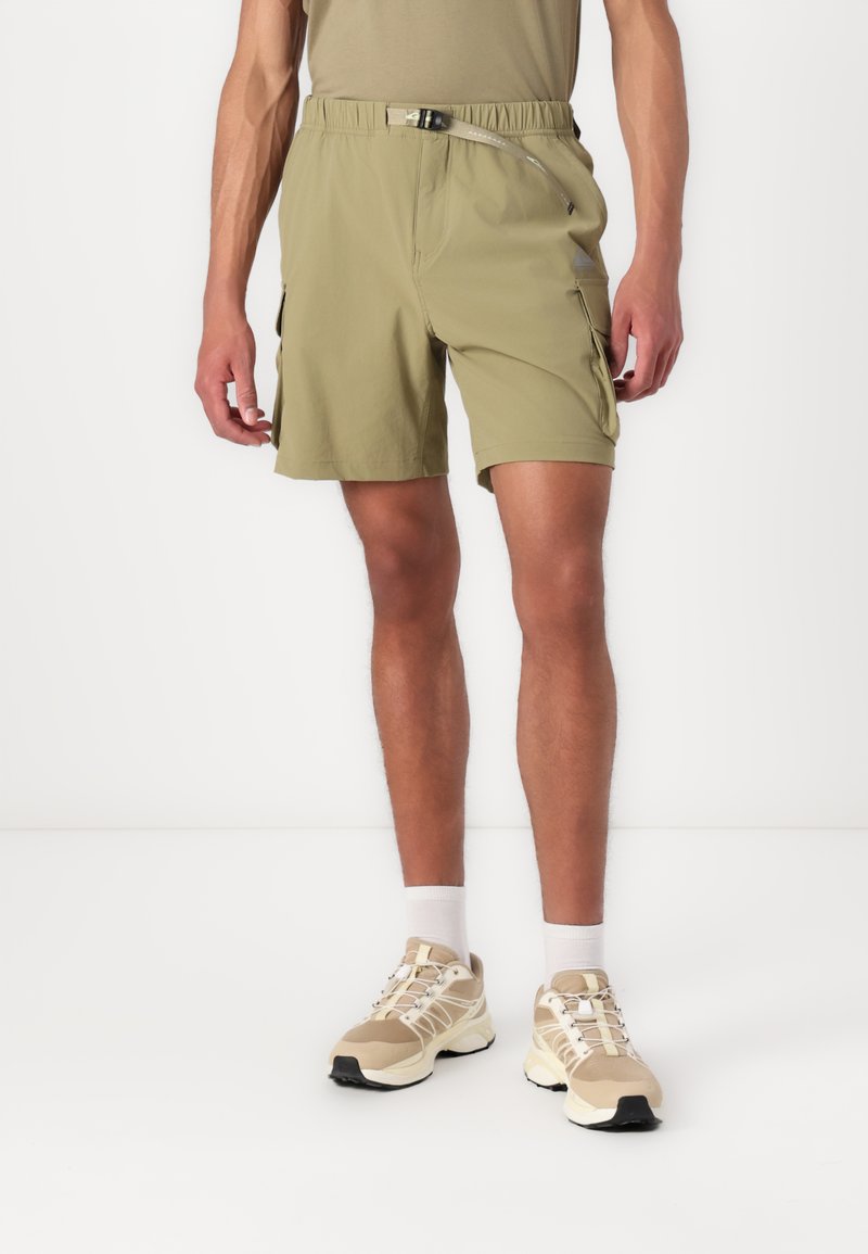 Lichtolijfgroene shorts met een elastische tailleband en riemdetail, voorzien van zijzakken. Gecombineerd met beige sneakers en witte sokken.