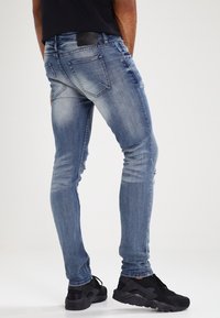 Chude niebieskie dżinsy o lekko wyblakłych miejscach i delikatnych przetarciach, z klasycznym pięciopocketowym designem i czarną metką na pasku.