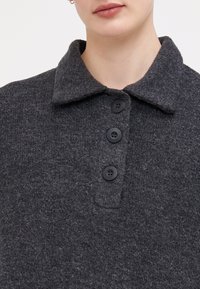 Polo shirt din lână gri, cu guler, trei nasturi negri și un material texturat, oferind un aspect confortabil.