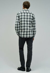 Camisa de cuadros en blanco y negro con mangas largas, diseño de botones y un dobladillo curvado, combinada con pantalones oscuros y zapatos negros.