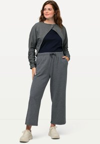 Cardigan largo gris texturizado de manga larga con cierre de presión sobre una camisa azul marino y pantalones gris con cordón a juego; combinado con zapatillas deportivas beige.