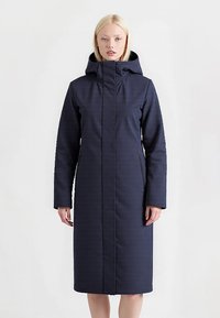 Marineblauwe pufferjas met hoge kraag en capuchon, heeft een rechte snit, twee verstelbare zakken en een gestructureerd exterieur.