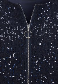 Tumesinine lukuga ülemine osa litritega, varustatud metallist luku ja ümmarguse tõmbega, kaunistatud erinevate siniste ja hõbedaste litritega.