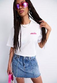 White cotton t-shirt with pink embroidered logo, paired with a blue denim mini skirt featuring frayed hem. Accessories include pink sunglasses.