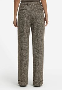 Vista posteriore di una persona che indossa pantaloni a gamba larga in tessuto a zig-zag marroni, con risvolti e tasche posteriori a scomparsa.