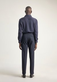 Camisa de manga larga de la marina con puños de botones, combinada con pantalones oscuros a medida. Textura suave, corte clásico y diseño minimalista.