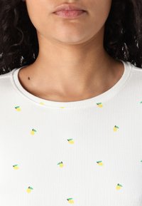 Witte ribbel-top met kleine gele citroenmotieven en groene accenten, ronde halslijn en korte mouwen. Gladde textuur.