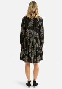 Sort kjole med lange ærmer, prydet med et blomsterprint i sølv. Lagdelt design med en løs pasform, parret med sorte sneakers.