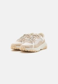 Beżowe sneakersy wykonane z połączenia zamszu i siateczki, z teksturowaną podeszwą, okrągłym noskiem i metalicznymi sznurowadłami z logotypem po bokach.