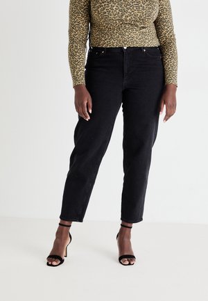 Frau trägt schwarze, hoch taillierte Jeans mit geradem Bein, langärmeliges Oberteil mit Leopardenmuster und schwarze Sandalen mit hohem Absatz und Knöchelriemen.