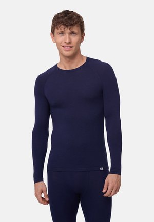 Haut thermique à manches longues bleu marine avec un col rond, coupe ajustée, texture lisse et poignets côtelés. Présente un petit détail de logo sur l'ourlet.