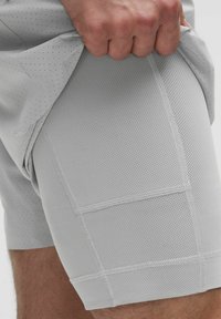 Hellgraue Sportshorts aus strukturiertem Mesh-Gewebe. Merkmale sichtbare Nähte und ein eng anliegendes Design, geeignet für aktive Bekleidung.