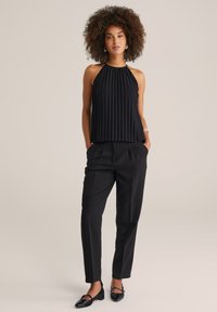 Čierny halter top s vertikálnymi záhybmi, skombinovaný s upravenými čiernymi nohavicami. Oblečenie sa vyznačuje hladkou textúrou a priliehavým strihom.