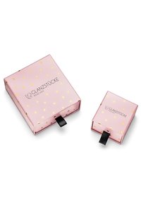 Två rosa förpackningslådor med guldprickiga mönster. Den större lådan har en logotyp och en svart dragrem; den mindre lådan har en liknande design och dragrem.