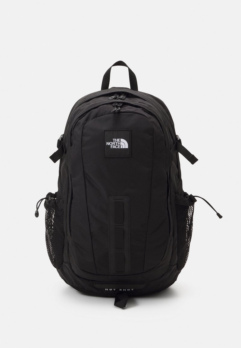 Sac à dos noir North Face Hot Shot avec plusieurs compartiments, patch logo à l'avant et poches latérales en mesh, présenté de face sur fond blanc.