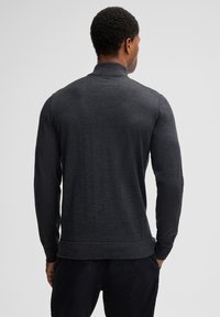 Dunkelgraues langärmliges Polohemd mit einer gleichmäßigen Strickstruktur und einem flachen Kragen. Das Hemd verfügt über einen gerippten Saum und gerippte Bündchen.