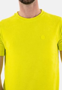 T-shirt à manches courtes, col rond, en tissu jaune néon vif. Présente un logo en relief discret sur la poitrine et une texture lisse.