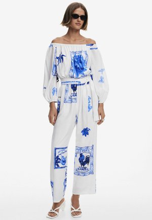 Top bianco senza spalle e pantaloni larghi coordinati con motivi stampati blu, tra cui foglie e galli. Dettaglio vita con cintura.
