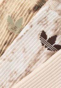 Tessuto lavorato a maglia in tonalità neutre con una texture a coste. Presenta motivi di foglie in verde e marrone su uno sfondo morbido.