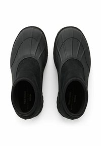 Svarta vattentäta skor med en slät, texturerad gummiyta och mockadetaljer, med en strömlinjeformad form och elastiska anklar.