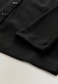 Schwarzes geripptes Langarmshirt mit einer Knopfleiste. Der Stoff hat eine subtile Textur; der Ärmel ist umgeschlagen und zeigt saubere Nähdetails.