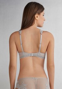 Szary biustonosz z koronkowym wykończeniem, z regulowanymi ramiączkami i zapięciem na haftkę z tyłu. Gładki materiał o subtelnym blasku i delikatnych detalach.