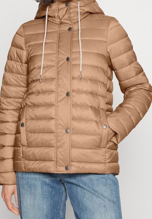 Béžová prošívaná bunda s kapucí na přední druky a boční kapsy, nošená s světlými modrými džínami.