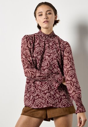 Blusa floreale bordeaux con maniche lunghe, scollatura arricciata e polsini smockati. Presenta un motivo paisley in rosa chiaro.