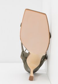 Chaussure à talons hauts en cuir vert avec un bout en amande, des côtés ouverts et un talon fin. Semelle plate de couleur claire avec une finition texturée.