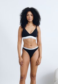 Crni bralett i tange set izrađen od mekanog materijala. Bralett ima podesive naramenice i bijelu elastičnu traku s brandom.