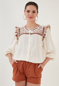 White blouse with colorful embroidery along the shoulders and neckline, featuring a button-up front and soft, flowy sleeves.