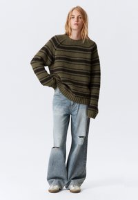 Olivengrønn stripete strikkegenser med en avslappet passform, kombinert med lyse, slitte denimjeans og sneakers. Myk tekstur og vide ben.