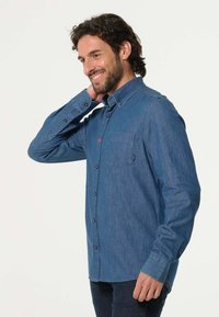 Denim overhemd in blauw, met lange mouwen, een borstzak en contrasterende rode knoopdetails. Glad textuur, getailleerde pasvorm.
