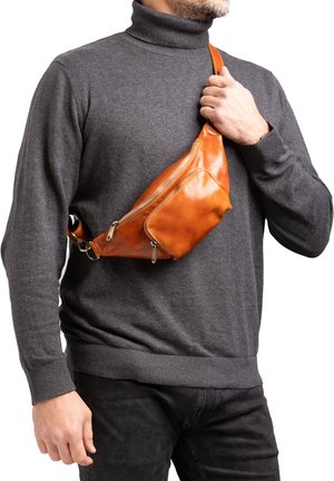 Uomo con maglione grigio a collo alto che indossa e tiene una marsupio marrone in pelle a tracolla con due tasche con cerniera.