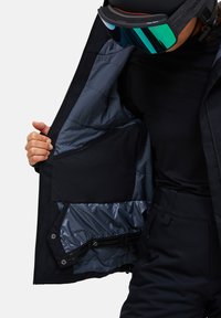 Giacca nera isolante con fodera blu-grigia, dotata di numerose tasche e una superficie liscia, aperta per rivelare i dettagli interni.