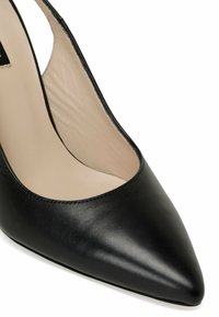 Chaussure à talon haut en cuir noir à bout pointu avec doublure intérieure beige, vue en gros plan sous un angle.
