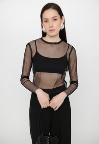 Haut noir transparent à manches longues en tissu mesh et au design semi-transparent, avec un col rond et une coupe slim.