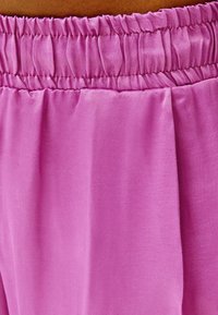 Losse, elastische broeken in helderroze stof, met een gladde textuur en een zachte val, voorzien van plooidetails.