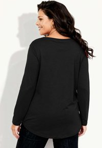 Czarna koszula z długim rękawem z zaokrąglonym dołem, wykonana z miękkiego materiału. Charakteryzuje się luźnym krojem i subtelnym upływem materiału z tyłu.