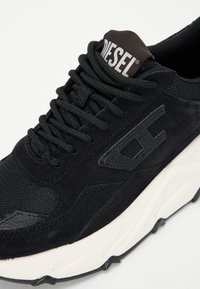 Black suede and mesh sneaker with textured accents, lace-up closure, and a white midsole. Features a "DIESEL" logo on the tongue.