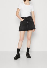 Černá džínová sukně do áčka s pěti kapsami a nesešitou spodní hranou, doplněná o přiléhavé bílé tričko a černé platformové boty s ponožkami.