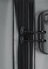 Close-up of a closed black zipper on textured silver hard-shell suitcase with dual zipper pulls secured by integrated lock.